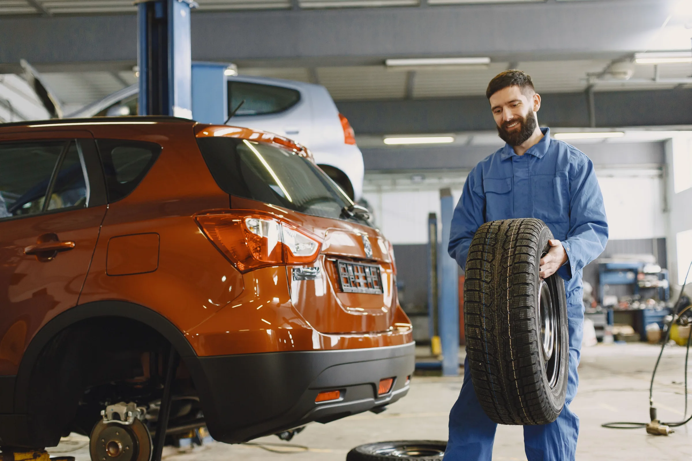 Mechanik drží zimní pneumatiku vedle vozu v dílně